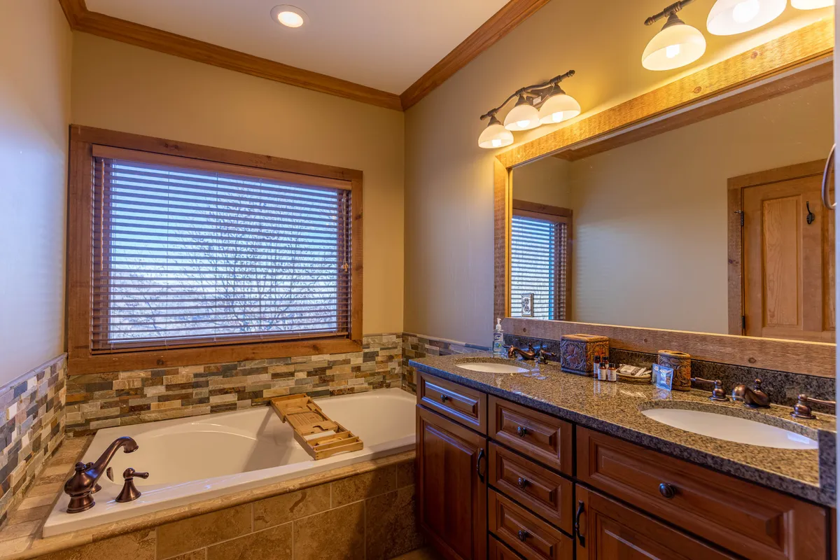 A serene and luxurious bathroom featuring a spacious bathtub, double sinks, a large mirror, and a window that brings in gentle natural light. The space is designed for relaxation and modern convenience.