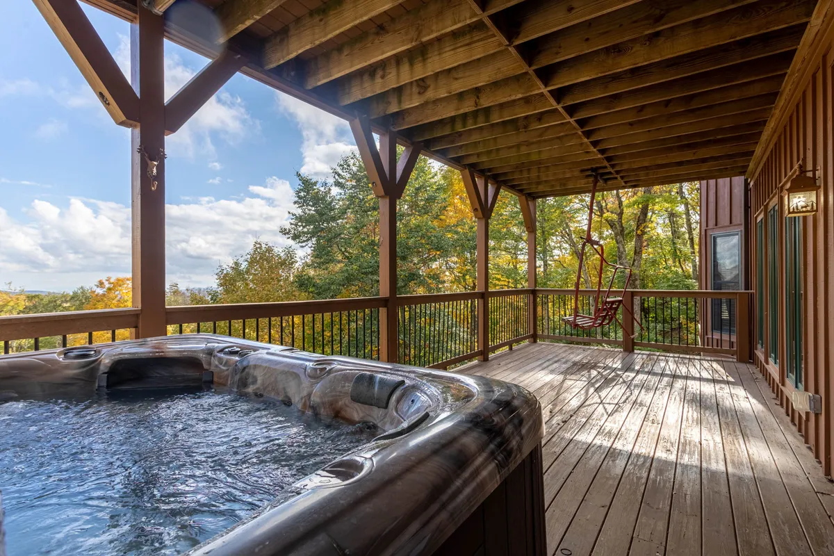 A wooden deck complete with a hot tub, swing seat, and surrounded by trees, offering a tranquil extension of the living space to the outdoors. It’s a setting for enjoying morning coffee or unwinding in the evening with friends and family.