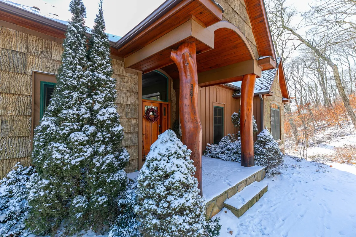 This image features the inviting front entrance of Buckhorn Lodge, adorned with wooden columns and snow-covered shrubs. A decorative wreath hangs on the door, setting a festive, wintry mood, and the porch area suggests a warm welcome after a day outdoors.