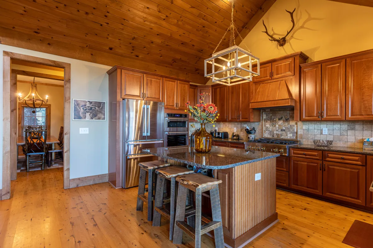 A warm, rustic kitchen with a central island, wooden cabinetry, and antler decor. The floral centerpiece adds a touch of homeliness, while the setup invites collaborative cooking and group meals. The space is clearly designed for social culinary experiences.