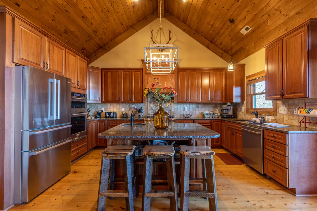 A chef-inspired kitchen featuring a granite island with wooden cabinetry, decorative chandelier, and stools. The space feels cozy and welcoming, ideal for casual breakfasts or preparing meals together.