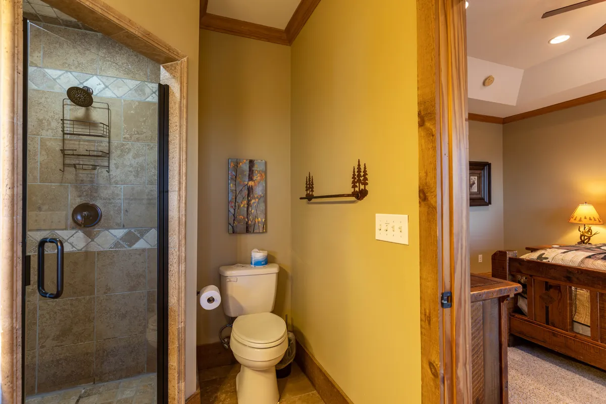 A tranquil bathroom scene with a modern shower area, toilet, eye-catching wall art, and a glimpse into an adjacent bedroom. The space feels airy and private, ideal for quiet self-care routines.