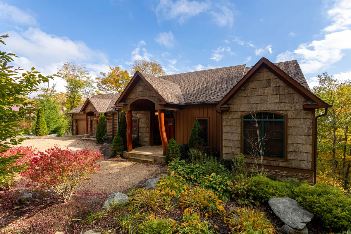 The image shows the front entrance of Buckhorn Lodge, featuring a landscaped garden and a stone pathway leading to a rustic wooden porch. The scene evokes a warm, inviting atmosphere and hints at spaces perfect for relaxing outdoors and enjoying mountain sunsets.
