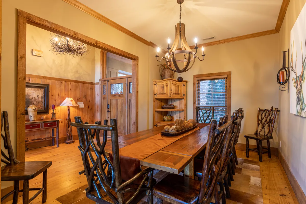 A large wooden dining table with rustic chairs and a chandelier above, set against a backdrop of decorative wall art. The scene is warm and welcoming, perfect for family meals and celebratory gatherings.