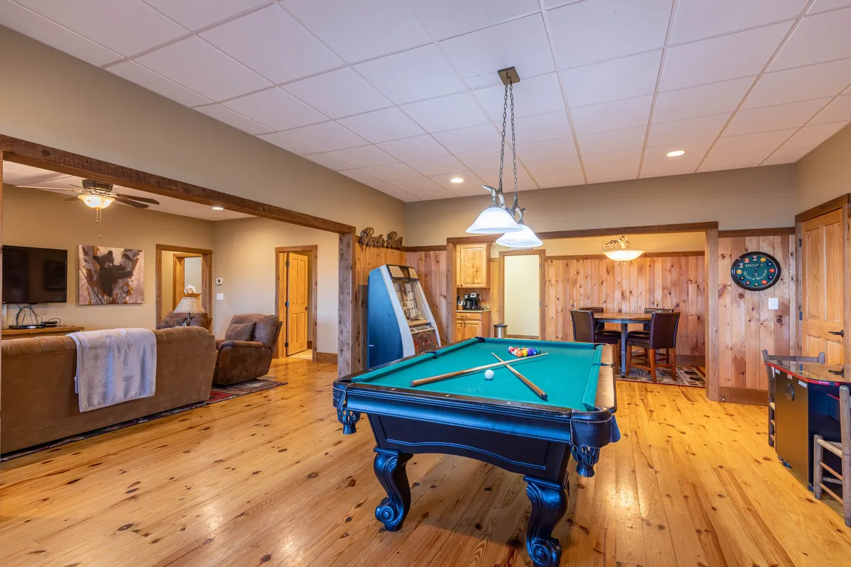 A cozy game room featuring a pool table at the center, with a sofa and dining table nearby. A vending machine adds to the fun, creating a vibrant, relaxed atmosphere perfect for gathering and entertainment.