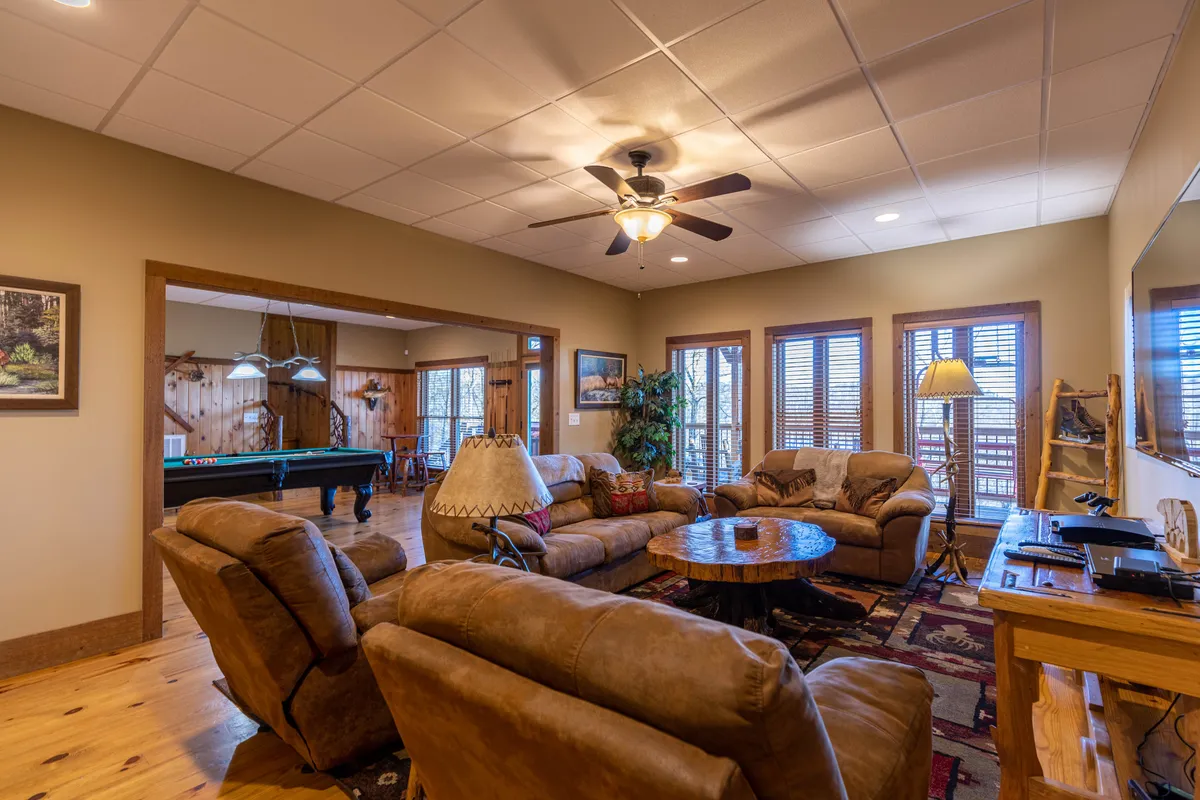 A welcoming lounge area with plush seating and a large coffee table, with a pool table visible in the adjoining room. Warm wooden accents and a decorative lamp create an inviting atmosphere ideal for relaxing and socializing between games.